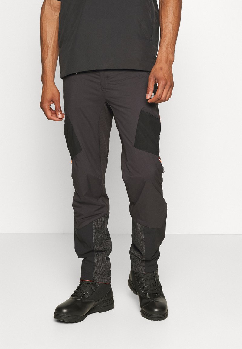 Svarte cargo-bukser med kontrasterende nylon-detaljer, mesh-paneler på nedre ben og oransje glidelåsdetaljer. Brukt med svarte snøreb boots.