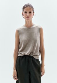 Beige top bez rukávů z měkké látky, s kulatým výstřihem a volným střihem, doplněný černými kalhotami s tkaničkami.