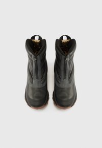 Par av svarta isolerade vinterstövlar med frontdragkedjor, dragflikar och bruna gummisulor, sedd uppifrån mot en vit bakgrund.