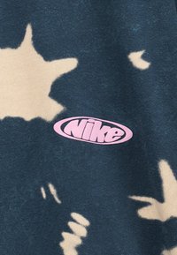 Σκούρο μπλε ύφασμα με μπεζ ανομοιόμορφα σχήματα και ένα ροζ οβάλ λογότυπο Nike τυπωμένο στο κέντρο.