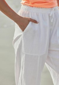 Pantalones de lino blancos con un ajuste holgado, que cuentan con una cintura con cordón y bolsillos laterales; textura suave con tela ligera y transpirable.