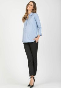 Light blue blouse with a collar and side pockets, paired with black slim-fit trousers. The outfit features a relaxed fit and smooth fabric.