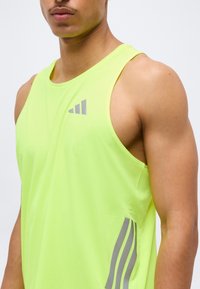 Άνδρας που φοράει φωτεινή κίτρινη αμάνικη αθλητική μπλούζα με γκρι λογότυπο και ρίγες, εμφανιζόμενος από το στήθος μέχρι το πάνω μέρος του βραχίονα.