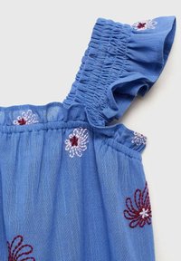 Blå bomullstopp med broderade blommönster i rött och vitt. Har volang, elastiska axelremmar och en mjuk, texturerad yta.