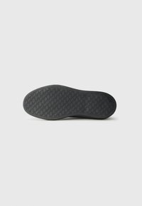 Suela de zapato de goma negra con un patrón de agarre texturizado que presenta líneas en zigzag y un tacón ligeramente elevado. Punta redondeada con un acabado suave.