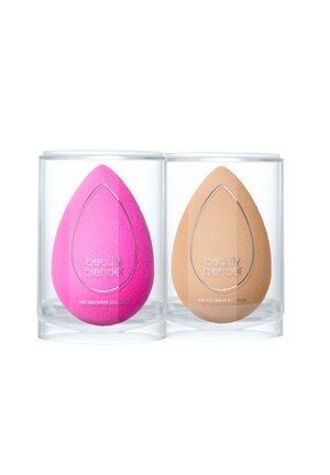Zwei Schönheitsschwämme in einem klaren zylindrischen Etui; einer ist leuchtend pink, der andere ist braun. Beide haben eine Tränenform und eine glatte Textur.