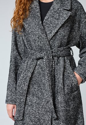 Sorte og hvide hørdesigns mønstret frakke med bælte, lavet af et struktureret stof. Har brede revers og sidelommer.