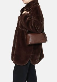 Cappotto in pelliccia sintetica marrone con una consistenza morbida, abbinato a una borsa a tracolla in pelle marrone con un design rettangolare semplice e un dettaglio in frange.