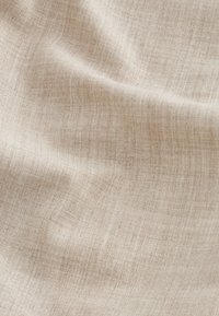Tessuto intrecciato beige chiaro con una texture sottile e pieghe morbide che creano ombre e luci delicate.