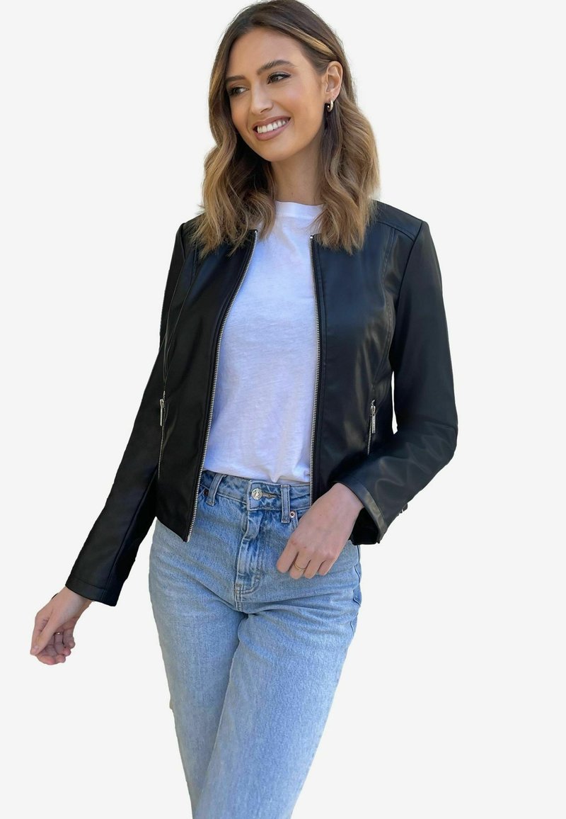 Black leather jacket with a fitted design, zip closure, and side pockets, worn over a white t-shirt and high-waisted light blue jeans.