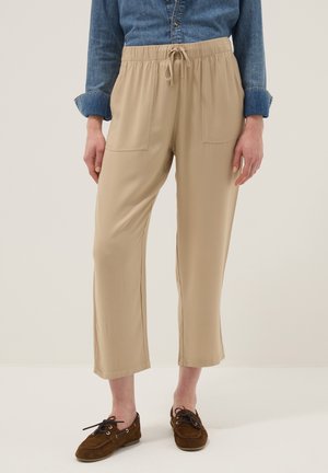 Mujer que lleva pantalones cortos beige con cordón y bolsillos delanteros, una camisa vaquera abotonada y mocasines marrones de ante con cordones.