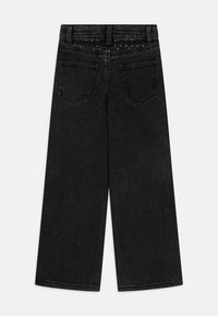 Jeans amplios negros con una textura de denim suave, que cuentan con bolsillos traseros y una línea decorativa de pequeños remaches a lo largo de la cinturilla.