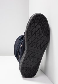 Námořnické sametové boty s texturovanou černou gumovou podrážkou, vybavené kovovými oky a šněrováním. Logo viditelné na podrážce.