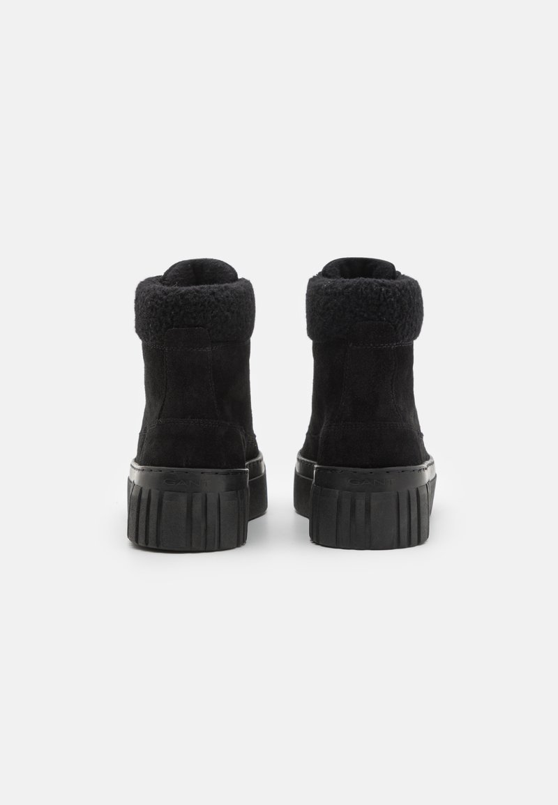 Schwarze Wildleder-Stiefeletten mit einem strukturierten schwarzen Kunstfellkragen, einer massiven schwarzen Gummisohle und vertikal gerippten Details an der Sohle.