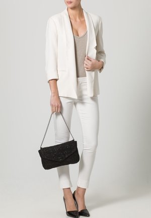 Biały żakiet na beżowej bluzce, w połączeniu z białymi spodniami. Czarna kopertówka z łańcuszkowym paskiem oraz czarne szpilki dopełniają całość.