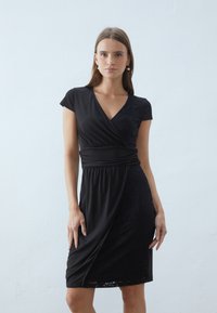 Black wrap dress featuring a V-neck, short cap sleeves, and a textured lace panel on one side; smooth fabric with a gathered waist detail.
