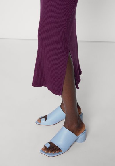 Sandálias de bico aberto azul claro com um salto grosso, apresentando uma tira larga e um pequeno laço para o dedo do pé. Usadas com um vestido roxo canelado.