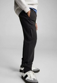 Svarta sweatpants i texturerat tyg med sidofickor och tapered design. Matchat med vita och grå sneakers.
