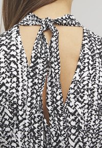 Black and white patterned top featuring a tied back detail with a keyhole cutout. Soft fabric, abstract design, and smooth texture evident.