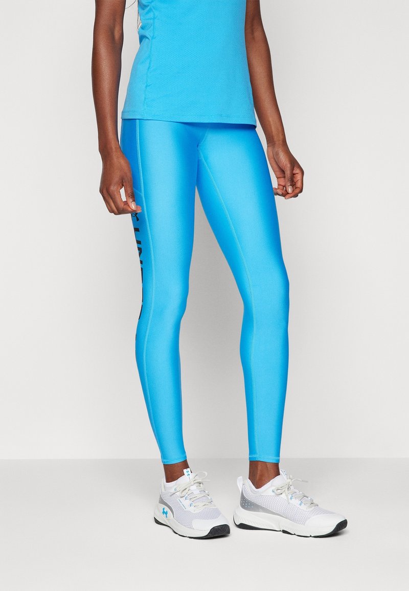 Osoba ubrana w jasnoniebieskie legginsy i pasujący bezrękawnik, stojąca w białych butach sportowych na jednolitym białym tle.