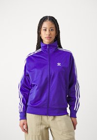 Giacca atletica viola con colletto alto, strisce bianche sulle maniche e logo ricamato sul petto. Tessuto liscio e lucido.