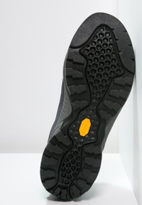 Czarna podeszwa buta z teksturowanym wzorem antypoślizgowym, z żółtym logo Vibram i gładkim, zakrzywionym krawędzią.