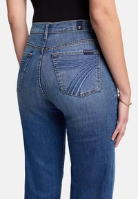 Dunkelblaue Jeans aus Denim mit hoher Taille, ausgestattet mit Gesäßtaschen mit geschwungenen Nähten und einem Logo-Tag über der rechten Tasche.