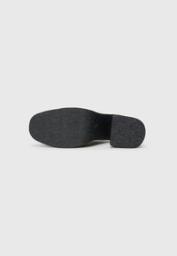 Talpa unei pantofi, realizată dintr-un material cauciucat texturat de culoare neagră, cu o formă rotundă; suprafața inferioară include o amprentă centrală și un model distinct.