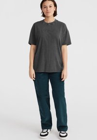 Grijze crewneck t-shirt met een relaxte pasvorm, met geborduurde branding. Gecombineerd met donkergroene corduroy broek en zwart-witte sneakers.