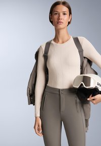 Bež dolgotrajni sloj z dolgimi rokavi z teksturiranim vzorcem diamantov, kombiniran s temno sivimi visokim pasom smučarskimi hlačami z zadrgnjami na žepih in zapiranjem na gumbe.