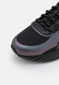 Chaussure de sport noire avec une tige en maille texturée, arborant un design irisé en dégradé sur la pointe et une semelle en caoutchouc noire contrastante.