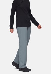 Lichtgrijze broek met een rechte pasvorm, discreet zijvak, gecombineerd met een zwart shirt met lange mouwen. Het materiaal lijkt zacht en duurzaam.