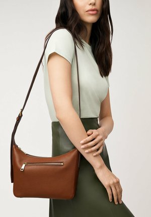 Sac en cuir marron à bandoulière avec une finition texturée, présentant une poche zippée à l'avant et une longue sangle sombre, exposé sur un fond neutre.