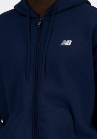 Navy zip-up hoodie made from soft fabric, featuring a kangaroo pocket, drawstrings, and a white New Balance logo on the chest.