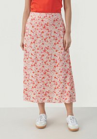 Gonna midi floreale in tessuto rosa chiaro, con fiori rossi e arancioni, linea dritta e texture liscia. Abbinata a sneakers bianche.