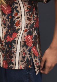 Chemise à motif floral beige, avec des accents rouge foncé et vert, dotée d'une fente ourlet et d'un tissu texturé.