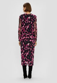 Zwarte jurk met roze en grijze abstracte patroon; doorzichtige lange mouwen, aansluitend silhouet, knielengte, gecombineerd met zwarte hoge hakken.
