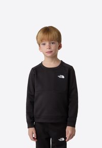 Musta collegepaita, jossa on pyöreä pääntie ja pitkät hihat, valkoinen logo rinnassa. Sileää kangasta, jossa on vain vähän ompelusaumoja.