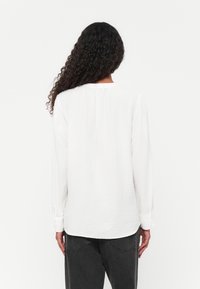 Witte blouse met lange mouwen van een textuurstof, ronde halslijn en knoopmanchetten, gecombineerd met donkergrijze tapered broeken.