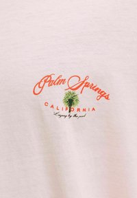 Κείμενο Palm Springs California με μικρό πράσινο γραφικό φοίνικα και τη φράση "Ξαπλωμένος δίπλα στην πισίνα" σε φωτεινό ύφασμα φόντου.