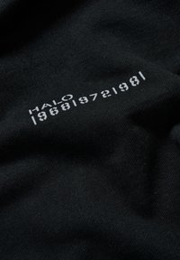 Czarna tkanina o gładkiej fakturze z białym nadrukowanym tekstem: "HALO 196819721981" w tłustej, nowoczesnej czcionce.