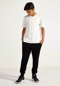 White short-sleeve v-neck t-shirt, black joggers with pockets, and black athletic shoes. Casual outfit with a relaxed fit.