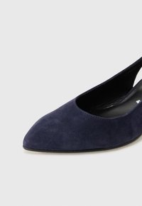 Chaussure slingback en suède bleu marine avec un bout pointu et des côtés découpés. Texture lisse et doublure intérieure noire. Design minimaliste.