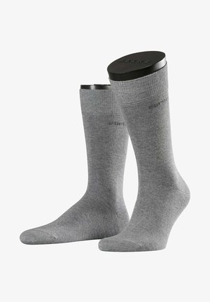 Chaussettes grises présentées debout. Texture lisse, longueur mi-mollet, bord élastique, avec un logo subtil sur un côté.