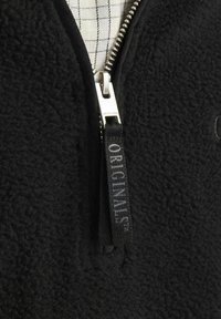 Sort fleece zip-up jakke med en struktureret overflade. Har en sølvfarvet lynlås og en sort stoftræksnor mærket "ORIGINALS." Inderlinningen er ternet.