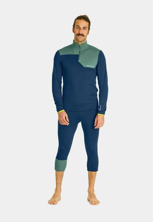 Navy and green athletic outfit featuring a long-sleeve top with a high collar and zip, paired with cropped leggings. Smooth, stretchy fabric.