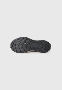 Trail shoe with a textured black rubber outsole featuring triangular lugs for traction. Light-colored upper with a flat, rounded toe design.