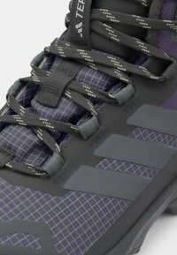 Purple hiking shoe featuring a textured gray upper, grid pattern, and reinforced overlays with reflective laces and subtle branding detail.