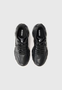 Svarte klumpete sneakers med tykke såler og snøring, merket "GUESS" inni skoene, vist fra oven på hvit bakgrunn.