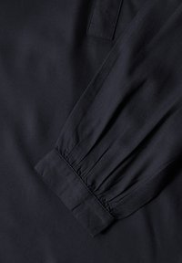 Dunkelnavy Blusenstoff mit gerafftem Ärmelbündchen. Glatte Textur mit subtiler glänzender Oberfläche und einem klaren, minimalistischen Design.